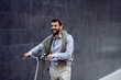 © Dusan Petkovic - Smiling cheerful caucasian fashionable businessman listening music and pushing his bicycle. In background is gray wall.