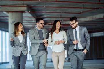 Four smiling positive successful business people visiting building in construction process.