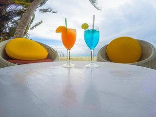 Two tropical fresh juices on white sandy beach.Exotic summer drinks , blur sandy beach on background.Fresh mojito cocktail on white table with blue sea as a background..Travel, Realaxation, Freshness