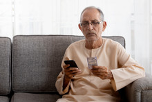 Senior Man Sitting On Couch Looking At Medicines And Checking On His Phone. (Health And Fitness) 
