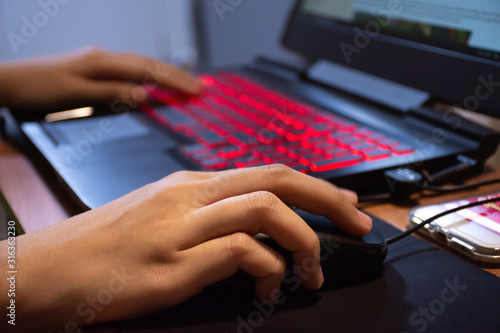 Close up woman hands using laptop computer are working or play game with red light LED backlit keyboard.