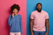 © Wayhome Studio - People and reaction concept. Smiling curious dark skinned woman and emotional shocked man stand next to each other, expresses happiness and surprisement, stand indoor over two colored background