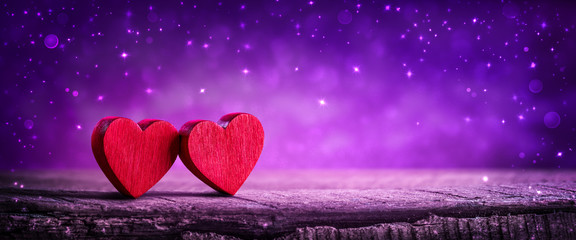 Wall Mural - two wooden hearts on rustic table with sparkling purple background - valentine's day concept