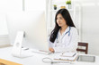 © Have a nice day  - Asian female doctor sitting at hospital office desk giving all patient convenience online service advice and smiling write a prescription on laptop to order medical,health care and preventing disease