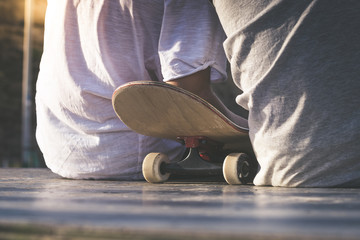 Wall Mural - Close up back view of two teens sitting on half pipe ramp with skateboard between them. Friendship at the skatepark.Youth togetherness, sport, joy, positive and carefree concept.