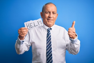 Senior handsome businessman holding paper help message over isolated blue background happy with big smile doing ok sign, thumb up with fingers, excellent sign