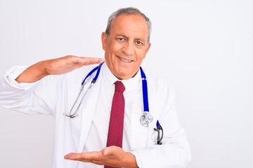 Sticker - Senior grey-haired doctor man wearing stethoscope standing over isolated white background gesturing with hands showing big and large size sign, measure symbol. Smiling looking at the camera. Measuring