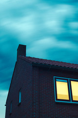 Poster - Spooky house with illuminated window under stormy sky at dusk.