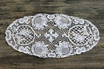 Openwork white lace napkin on a rough dark wooden background close up