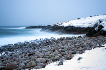 Wall Mural - long exposure of surf breaking on snow covered rocky shores and large stone boulders in the polar re