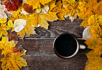 Wall Mural - Hot coffee in an enamel mug with autumn maple leaves on wooden background. Autumn cozy background. Top view. Copy space.