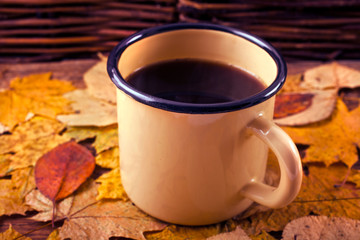 Wall Mural - Hot coffee in an enamel mug on a background of leaves. Autumn cozy background.