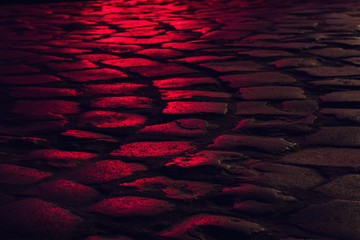 Wet illuminated by red light cobblestone street at night