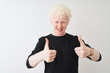 © Krakenimages.com - Young albino blond man wearing black t-shirt standing over isolated white background success sign doing positive gesture with hand, thumbs up smiling and happy. Cheerful expression and winner gesture.