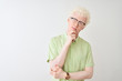 © Krakenimages.com - Young albino blond man wearing green shirt and glasses over isolated white background with hand on chin thinking about question, pensive expression. Smiling with thoughtful face. Doubt concept.