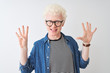 © Krakenimages.com - Young albino blond man wearing denim shirt and glasses over isolated white background showing and pointing up with fingers number nine while smiling confident and happy.