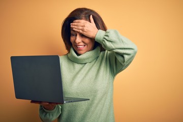 Poster - Middle age brunette woman using computer laptop over yellow background stressed with hand on head, shocked with shame and surprise face, angry and frustrated. Fear and upset for mistake.