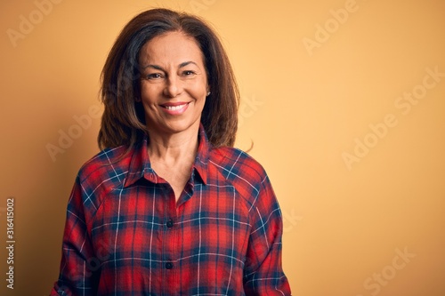 Fotografía Middle age beautiful woman wearing casual shirt standing over isolated yellow background with a happy and cool smile on face