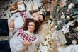 © Tetiana Moish - Young sensual couple in love in cold winter new year evening laying on the warm carpet near christmas tree. Stylish couple, guy and girl in sweaters with hearts. Girl with beautiful makeup and afro cu