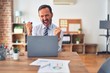 © Krakenimages.com - Middle age handsome businessman wearing tie sitting using laptop at the office very happy and excited doing winner gesture with arms raised, smiling and screaming for success. Celebration concept.