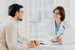 © VK Studio - Attentive female doctor explains diagnosis to patient, gives professional consultancy, points with pen at laptop, talk about health concerns, pose at private clinic in modern office, show prescription