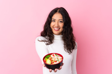 Wall Mural - Mixed race woman holding a bowl full of noodles over isolated pink background with happy expression