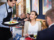 © JackF - Waiter with dishes serving man and woman friendly company indoors