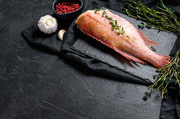 Raw red sea perch on a stone Board with thyme. Black background. Top view. Space for text