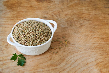 Canvas Print - Raw green lentils in a white bowl on a wooden background 