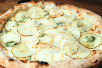 Wall Mural - Freshly baked pizza with cheese, sauce, and pear on a wooden table close up