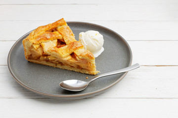 Piece of an apple pie with ice cream on white wooden table. Shallow focus.