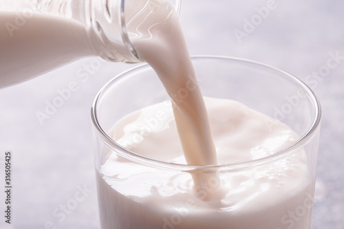 Fotografía Pouring milk from bottle into a glass on light blue background, high key shot