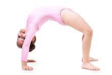 Small positive girl in pink gymnastic jumpsuit standing in bridge pose and smiling over white background