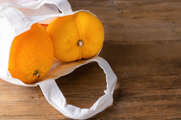 Two citrus in white fabric bag, one Ugly double lemon, and normal orange on wooden textured surface. Buying imperfect product to reduce food waste. Horizontal. Cooking. Eco trend