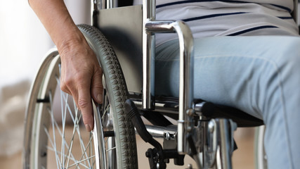 Wall Mural - Close up disabled older woman sitting in wheelchair, touching wheels