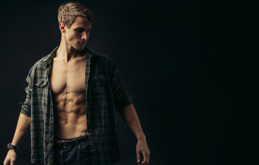 young caucasian man with muscular strong body opened torso, checkered casual shirt on him, he looks side isolated over black background