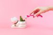 © _KUBE_ - Green cactus in a white flowerpot like cat and a woman's hand holding a razor on a pink background. The concept of depilation, epilation and removal unwanted hair on the body. Copy space