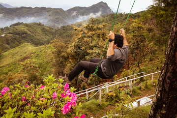 Joven en un columpio con flores al rededor en la montaña