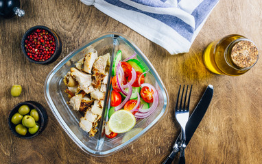 Wall Mural - Healthy lunch box with chicken, tomatoes, cucumbers, olive and onion on wooden table. Top view