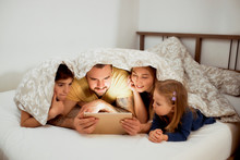 Beautiful Caucasian Family Lying On Bed Together Under Blanket,wearing Casual Wear, Have Free Time At Morning, Watching Video Or Film On Tablet