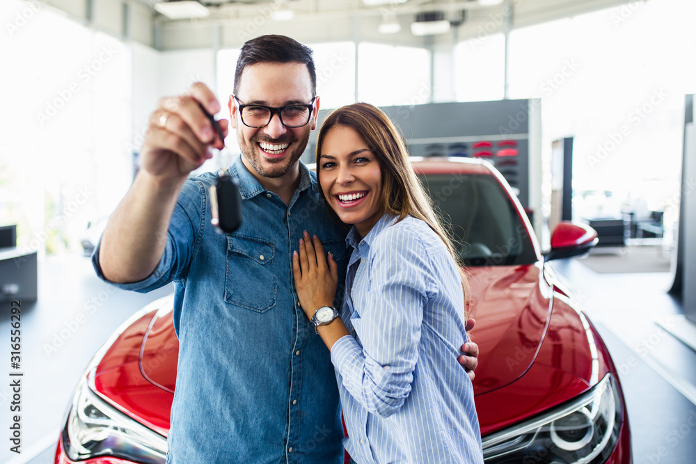 Beautiful young smiling couple holding a key of their new car.