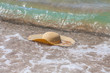Wicker straw hat floating in water near the seashore in sea waves