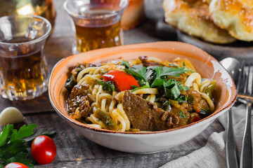 Wall Mural - Traditional asian uzbek noodle lagman with vegetables and meat on rustic wooden table background. Close-up