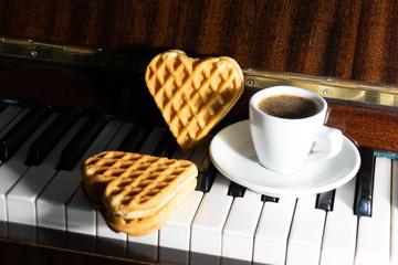 Cup of coffee and two lovely heart shaped waffles on piano keys background