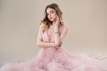 Attractive Young Woman Portrait In Tender Pink Lace Dress Sits On Beige Background In Studio