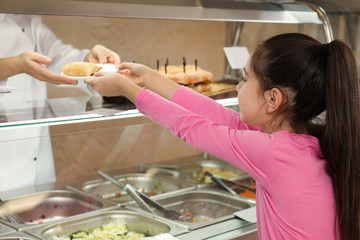 Woman giving plate with tasty food to girl in school canteen