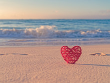 Tropical Background For St. Valentine's Day. A Red Wicker Heart Is Located On A Sandy Beach. Behind Is The Sea Or Ocean. Love Of Travel.