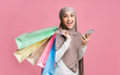 © Prostock-studio - Cheerful arabic woman in veil holding smartphone and bright paper bags