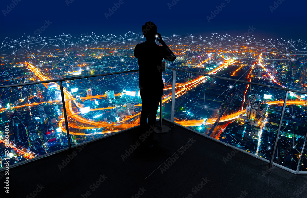 Businessman standing using smart phone in modern space watching city night view.Business Wireless network and Connection technology concept. - obrazy, fototapety, plakaty 