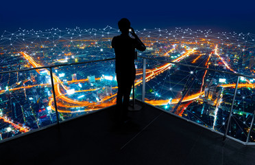 Fototapete - Businessman standing using smart phone in modern space watching city night view.Business Wireless network and Connection technology concept.